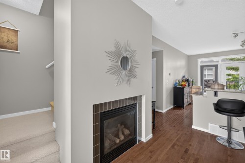 Gas fireplace with a tile surround, hardwood flooring, and a breakfast bar with a stone countertop - #53 603 Watt Bv Sw, Edmonton, AB - Indoor Photo Showing Living Room With Fireplace