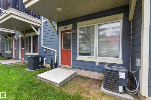 Blue horizontal siding exterior with a red entry door, white trim windows, and an outdoor HVAC unit - #53 603 Watt Bv Sw, Edmonton, AB - Outdoor