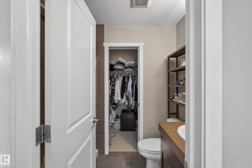 Bathroom featuring a built-in wood-finish vanity with an integrated sink, a toilet, and an open closet area with shelving and hanging storage - #53 603 Watt Bv Sw, Edmonton, AB - Indoor Photo Showing Bathroom