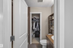 Bathroom featuring a built-in wood-finish vanity with an integrated sink, a toilet, and an open closet area with shelving and hanging storage - 