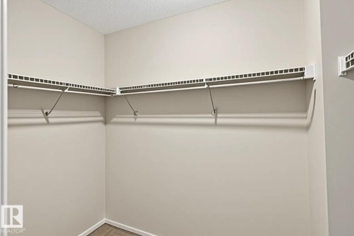 Built-in closet shelving system with white wire racks and hanging rods, beige wall paint, and wood-finish flooring - #53 603 Watt Bv Sw, Edmonton, AB - Indoor With Storage
