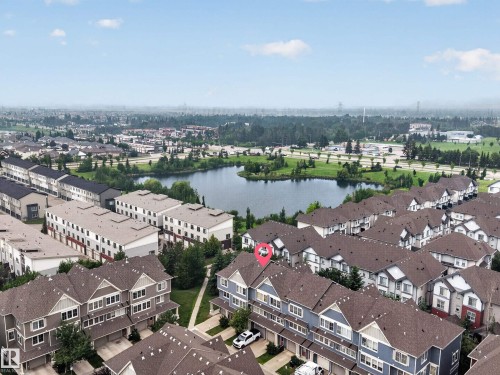Aerial perspective showcasing a community of townhomes with pitched roofs and light-colored siding - #53 603 Watt Bv Sw, Edmonton, AB - Outdoor With Body Of Water With View