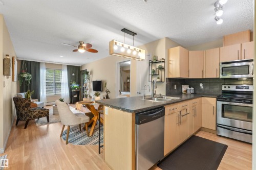 Kitchen featuring stainless steel appliances, light wood-finish cabinetry, and dark countertops - #209 103 Ambleside Drive Sw, Edmonton, AB - Indoor Photo Showing Kitchen With Double Sink