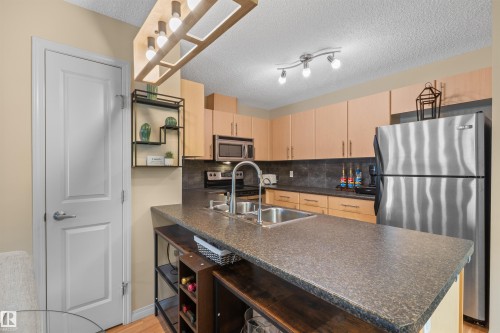 Kitchen featuring stainless steel appliances, light wood-finish cabinetry, dark countertop, and track lighting - #209 103 Ambleside Drive Sw, Edmonton, AB - Indoor Photo Showing Kitchen With Double Sink