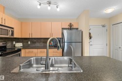 Kitchen featuring a stainless steel double-basin sink, dark stone-finish countertops, light wood-finish cabinetry, stainless steel appliances, and track lighting - 
