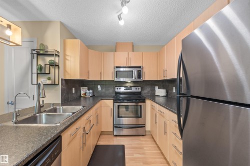 U-shaped kitchen featuring wood-finish cabinetry, stainless steel appliances, dark countertops, and a tile backsplash - #209 103 Ambleside Drive Sw, Edmonton, AB - Indoor Photo Showing Kitchen With Double Sink With Upgraded Kitchen
