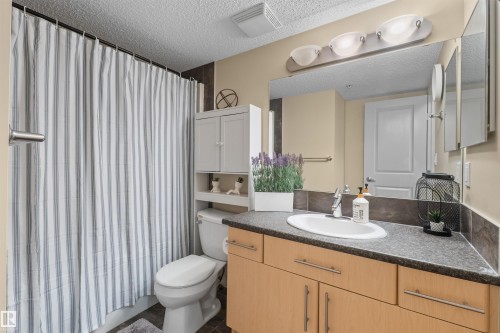 Bathroom featuring a single vanity with an integrated sink, wood-finish cabinetry, and a full-width mirror - #209 103 Ambleside Drive Sw, Edmonton, AB - Indoor Photo Showing Bathroom