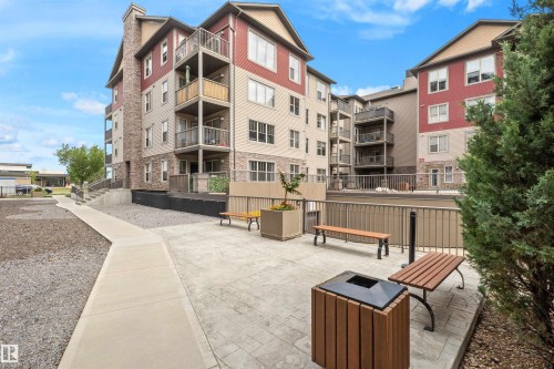 Multi-story building featuring balconies, stone accents, and a paved courtyard with benches - #209 103 Ambleside Drive Sw, Edmonton, AB - Outdoor