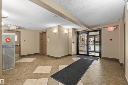 Tiled flooring with a diamond pattern, neutral wall paint, overhead lighting, wall sconces, and double glass entry doors - #209 103 Ambleside Drive Sw, Edmonton, AB - Indoor