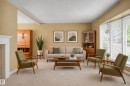 Living area featuring carpeting, large windows with blinds, a white mantel, and ceiling with a vaulted element - 10715 50 Street Nw, Edmonton, AB 