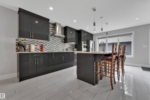 Modern kitchen featuring dark glossy cabinetry, stainless steel appliances, a mosaic tile backsplash, and a central island with pendant lighting - 9329 Connors Road Nw, Edmonton, AB - Indoor Photo Showing Kitchen With Upgraded Kitchen