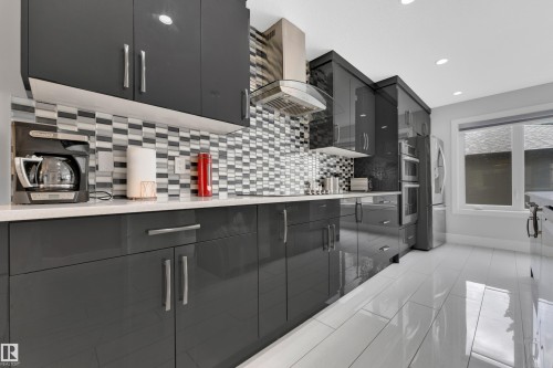 Contemporary kitchen featuring glossy dark cabinetry, a mosaic tile backsplash, and a stainless steel range hood - 9329 Connors Road Nw, Edmonton, AB - Indoor Photo Showing Kitchen