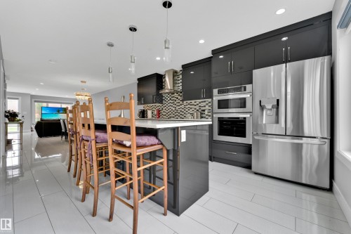 Kitchen island with white countertop, dark cabinetry, stainless steel appliances, and a mosaic tile backsplash - 9329 Connors Road Nw, Edmonton, AB - Indoor Photo Showing Kitchen With Upgraded Kitchen