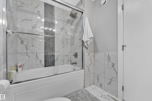 Bathtub with glass sliding doors, featuring a tiled surround with a vertical mosaic accent - 9329 Connors Road Nw, Edmonton, AB - Indoor Photo Showing Bathroom