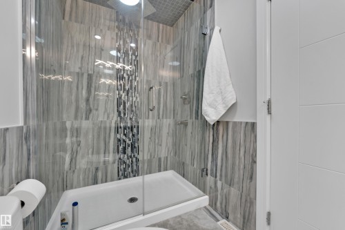 Walk-in shower featuring glass enclosure, gray veined tile walls, and a mosaic tile accent strip - 9329 Connors Road Nw, Edmonton, AB - Indoor Photo Showing Bathroom