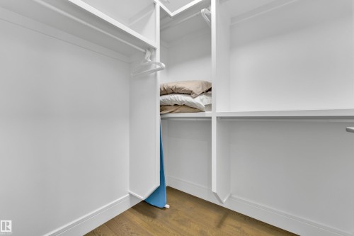 Integrated closet system featuring white shelving, multiple hanging rods, and wood-finish flooring - 9329 Connors Road Nw, Edmonton, AB - Indoor With Storage