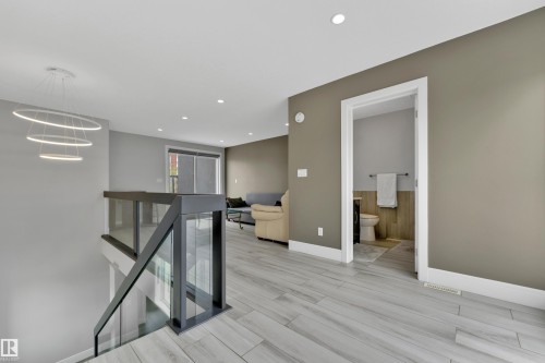 Modern open-concept upper level featuring sleek glass and metal railings, contemporary circular pendant lighting, wood-finish flooring, recessed ceiling lights, and a convenient powder room - 9329 Connors Road Nw, Edmonton, AB - Indoor Photo Showing Other Room