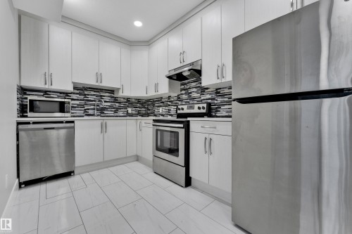 Contemporary kitchen featuring white cabinetry, stainless steel appliances, a mosaic tile backsplash, white countertops, and light-toned tile flooring - 9329 Connors Road Nw, Edmonton, AB - Indoor Photo Showing Kitchen With Upgraded Kitchen