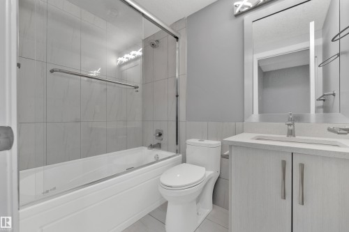 Bathroom featuring a tub and shower combination with glass enclosure, white tile surround, and a coordinating vanity with a light countertop and undermount sink - 9329 Connors Road Nw, Edmonton, AB - Indoor Photo Showing Bathroom