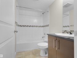 White tile surround shower-tub combination, mosaic tile accent, wood-finish vanity with countertop, oval undermount sink, and tile flooring - 