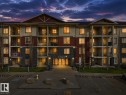 Multi-story building featuring balconies, stone veneer accents, and an integrated parking area - #220 5804 Mullen Pl Nw, Edmonton, AB  - Outdoor With Balcony With Facade 
