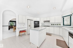 White shaker cabinetry, recessed lighting, tile flooring, kitchen island with glass top, and a built-in desk area - 