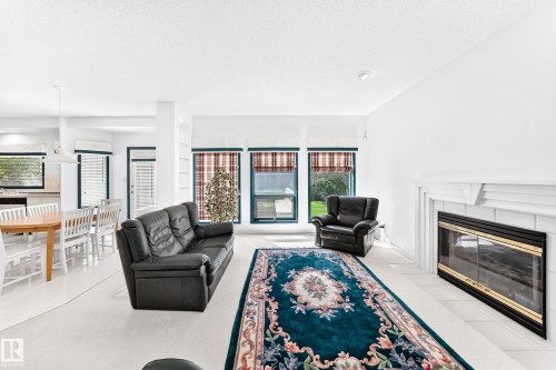 Living area featuring a fireplace with a white mantel, large windows with blinds, and white wall finishes - 209 Carmichael Close Nw, Edmonton, AB - Indoor Photo Showing Living Room With Fireplace