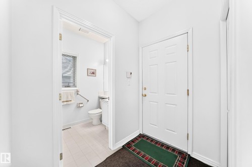 White panel door, light-colored tile flooring, window with horizontal blinds, built-in toilet, and wall-mounted vanity with a sink - 209 Carmichael Close Nw, Edmonton, AB - Indoor Photo Showing Other Room
