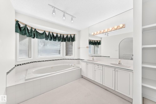 Deep soaking tub, dual vanity with undermount sinks, track lighting, built-in shelving, and a large wall mirror - 209 Carmichael Close Nw, Edmonton, AB - Indoor Photo Showing Bathroom