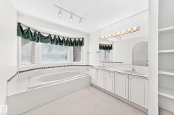 Deep soaking tub, dual vanity with undermount sinks, track lighting, built-in shelving, and a large wall mirror - 