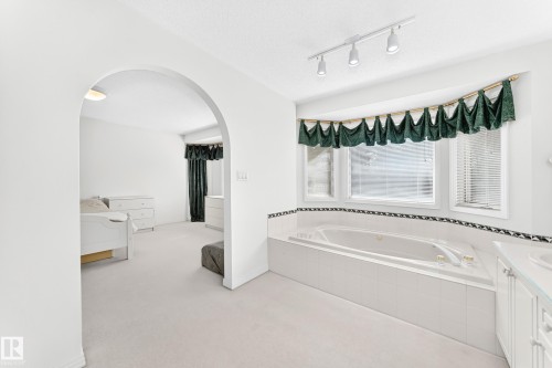 Soaking tub with tiled surround, bay window, track lighting, and an arched entry - 209 Carmichael Close Nw, Edmonton, AB - Indoor Photo Showing Bathroom