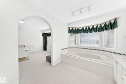 Soaking tub with tiled surround, bay window, track lighting, and an arched entry - 