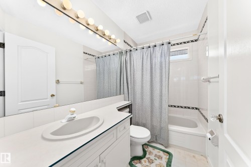 White tile tub/shower combination, vanity with integrated sink, wall-mounted mirror, and decorative tile accents - 209 Carmichael Close Nw, Edmonton, AB - Indoor Photo Showing Bathroom