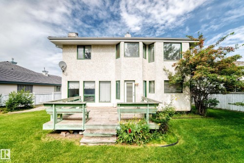 Rear exterior featuring a two-story stucco finish, multiple windows with green trim, a wooden deck, and a manicured lawn - 209 Carmichael Close Nw, Edmonton, AB - Outdoor