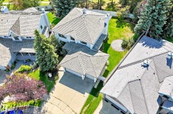 White multi-story residence with a gray shingle roof, attached two-car garage, expansive concrete driveway, and mature landscaping - 