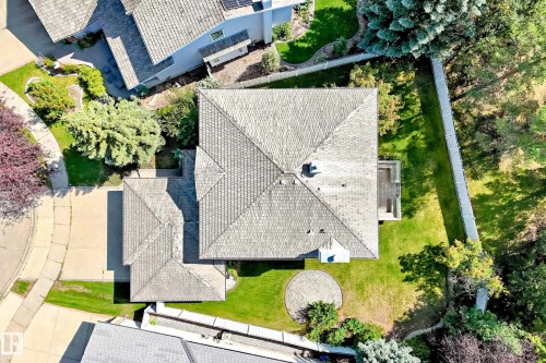 Expansive property featuring a multi-pitched roofline, lush green lawn, mature trees, concrete driveway, and a circular paved patio area - 209 Carmichael Close Nw, Edmonton, AB - Outdoor