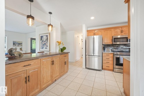 Kitchen featuring a breakfast bar with pendant lighting, light wood cabinetry, stainless steel appliances, and tile flooring - 16613 90 Avenue Nw, Edmonton, AB - Indoor Photo Showing Kitchen