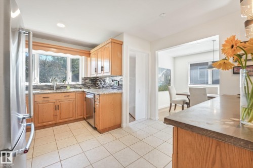 Kitchen featuring wood-finish cabinetry, stainless steel appliances, granite countertops, and a tile backsplash - 16613 90 Avenue Nw, Edmonton, AB - Indoor Photo Showing Kitchen