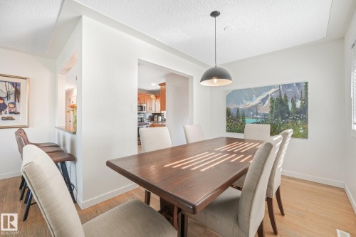 Light-toned wood-finish flooring, a contemporary pendant light fixture, and a pass-through bar with seating - 16613 90 Avenue Nw, Edmonton, AB - Indoor Photo Showing Dining Room
