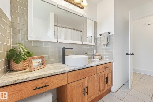 Wood-finish vanity with ample storage, light-toned countertop, and vessel sink - 16613 90 Avenue Nw, Edmonton, AB - Indoor Photo Showing Bathroom