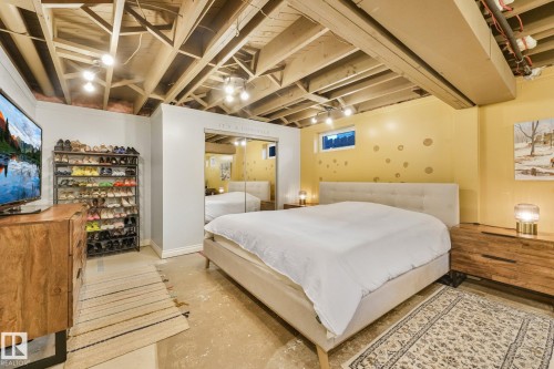 Exposed ceiling joists with track lighting, mirrored closet doors, a built-in wall niche, and a neutral-toned bed frame with a padded headboard - 16613 90 Avenue Nw, Edmonton, AB - Indoor Photo Showing Bedroom