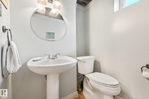 Pedestal sink with chrome faucet, round wall mirror, and overhead vanity lighting - 16613 90 Avenue Nw, Edmonton, AB - Indoor Photo Showing Bathroom
