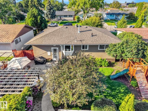 Backyard featuring a concrete patio, a wooden pergola, a playset with a slide, a curved concrete pathway, and mature landscaping - 16613 90 Avenue Nw, Edmonton, AB - Outdoor