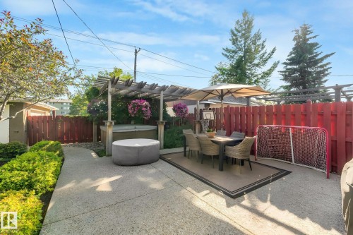 Paved patio area featuring a hot tub beneath a wooden pergola, an outdoor dining set with an umbrella, and a privacy fence - 16613 90 Avenue Nw, Edmonton, AB - Outdoor