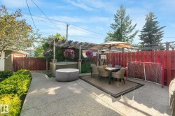 Paved patio area featuring a hot tub beneath a wooden pergola, an outdoor dining set with an umbrella, and a privacy fence - 