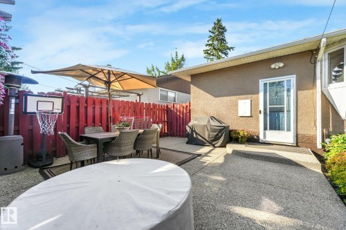 Expansive concrete patio area with a red privacy fence and exterior door access - 16613 90 Avenue Nw, Edmonton, AB - Outdoor With Deck Patio Veranda With Exterior