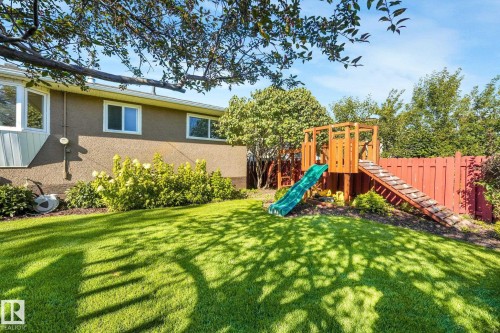 Expansive backyard with a manicured lawn, established landscaping, and a built-in wooden play structure with a slide - 16613 90 Avenue Nw, Edmonton, AB - Outdoor