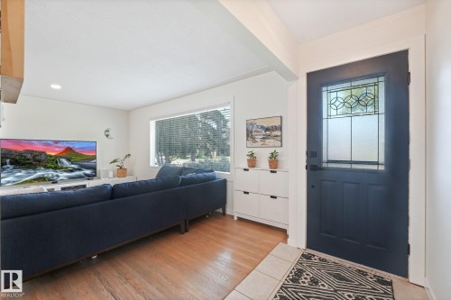 Entryway featuring a dark paneled door with decorative glass, tile flooring, and wood-finish flooring extending into the living area - 16613 90 Avenue Nw, Edmonton, AB - Indoor Photo Showing Other Room