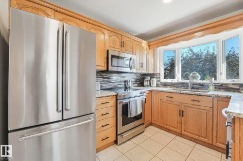 Kitchen featuring oak cabinetry, stainless steel appliances, granite countertops, tile flooring, and a bay window - 16613 90 Avenue Nw, Edmonton, AB - Indoor Photo Showing Kitchen