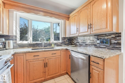 Bay window, granite countertops, wood cabinetry, tile backsplash, stainless steel dishwasher - 16613 90 Avenue Nw, Edmonton, AB - Indoor Photo Showing Kitchen